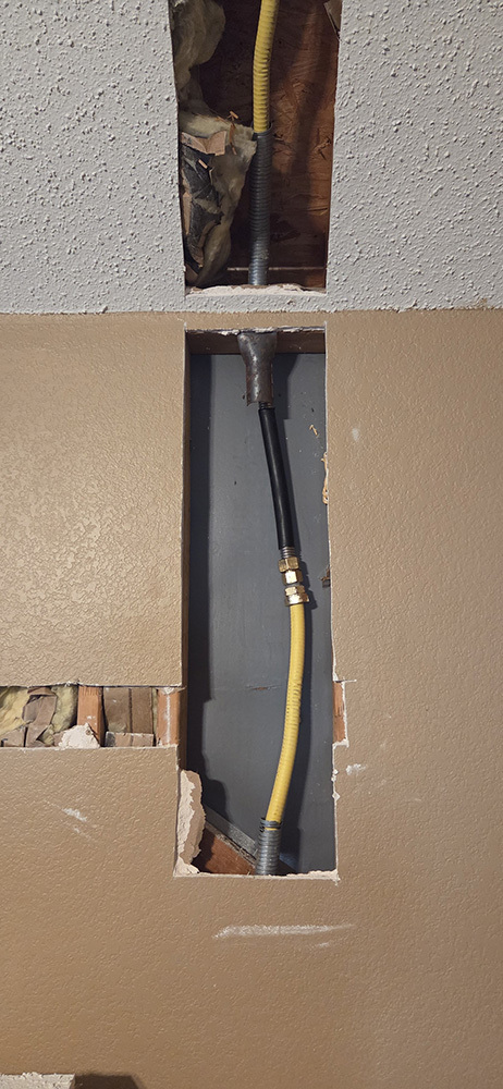 Repaired gas line leak inside the wall using yellow gas tubing for a safe, secure connection.