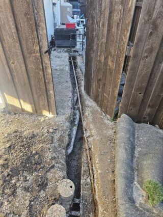 New gas line installation in narrow trench between wooden fence panels at Frisco home, showing poly piping and proper grading.
