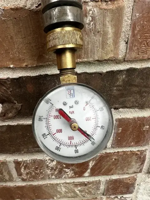 Pressure gauge mounted on brick wall showing water pressure measurement during hydrostatic sewer testing