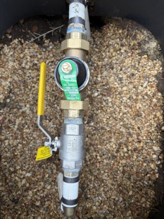 Newly installed pressure reducing valve on copper plumbing pipe with yellow ball valve handle and green regulation label.