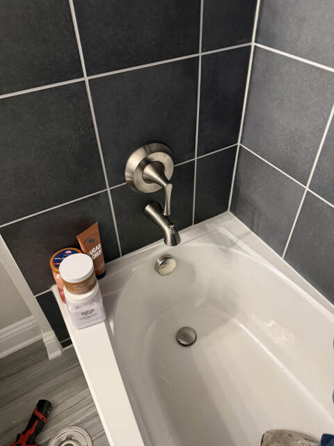 Modern brushed nickel shower trim installed above white bathtub with black subway tile walls in Frisco bathroom remodel
