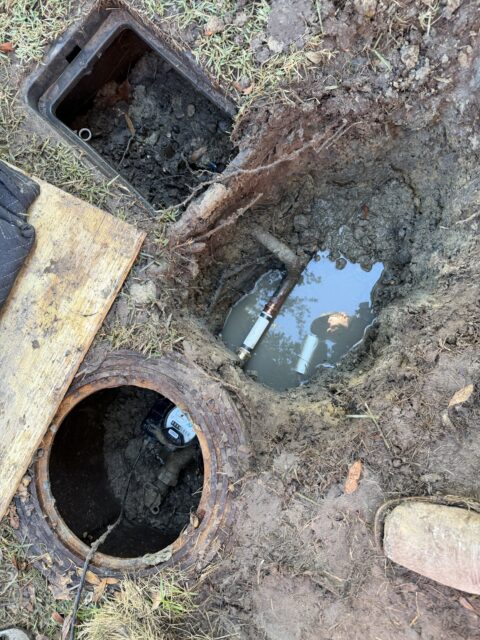 Exposed water main pipe with failed tee fitting and repair materials visible in excavated trench in Frisco yard
