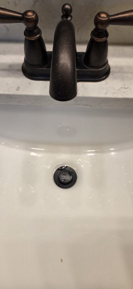 Completed installation of oil-rubbed bronze pop-up drain assemblies in the master bathroom sinks.