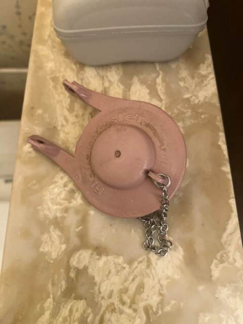 Pink drain stopper with chain attachment displayed on textured countertop surface