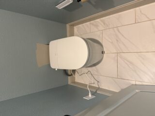 Modern white Moen smart toilet with bidet and heated seat installed in Frisco bathroom with marble tile backsplash