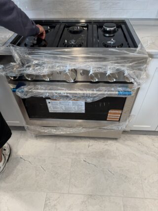 New stainless steel gas range wrapped in protective plastic during Frisco kitchen remodel installation