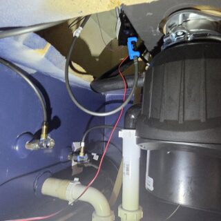 Under-sink garbage disposal and plumbing connections installed in a kitchen, showing proper drain setup and electrical wiring