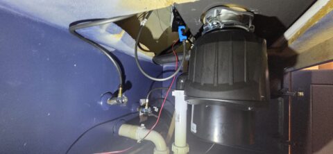 Under-sink garbage disposal and plumbing connections installed in a kitchen, showing proper drain setup and electrical wiring
