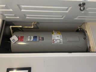 New electric water heater installed in garage ceiling cavity with brass connections and safety labels visible