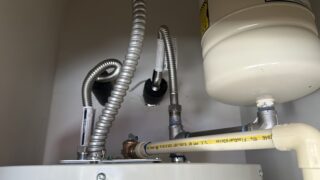 New electric water heater installation in Frisco home showing connected supply lines and drain pan setup