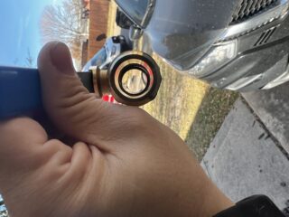 Technician holding a new brass ball valve with red handle next to a water heater drain in Frisco, TX