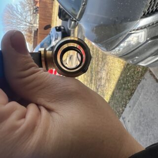 Technician holding a new brass ball valve with red handle next to a water heater drain in Frisco, TX