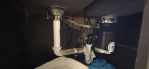 Under-sink plumbing installation showing white P-trap pipes and basket strainer assembly in Frisco home
