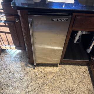Stainless steel Perlick bar refrigerator installed under granite countertop with water filter system visible below sink in Frisco home