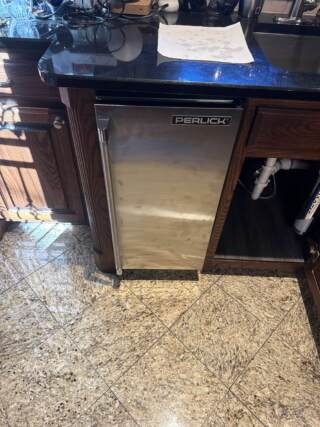 Stainless steel Perlick bar refrigerator installed under granite countertop with water filter system visible below sink in Frisco home